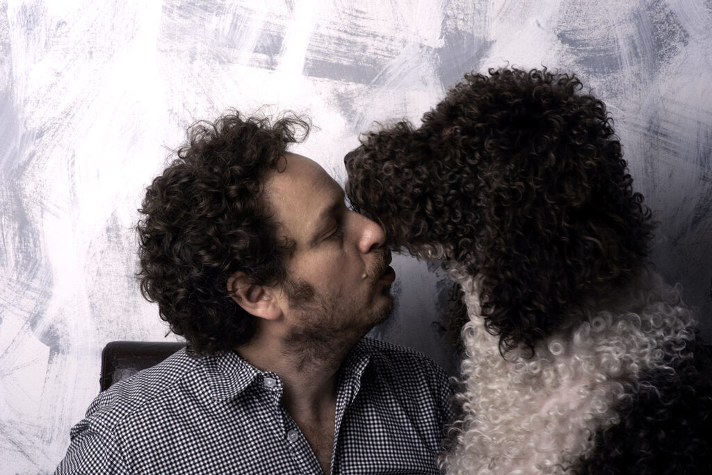 Artist Gregg Brown in a tender moment with his brown and white Labradoodle, Roman, in front of a grey and white abstract painting by Gregg.